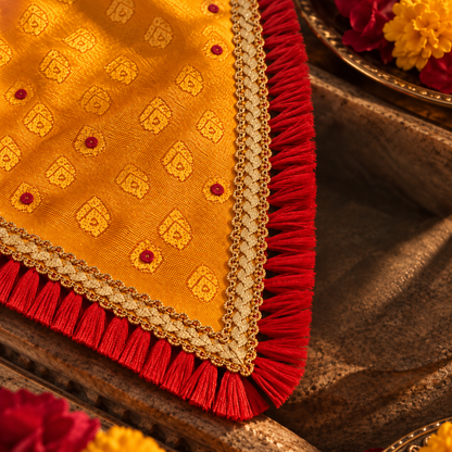Close-up of mustard-yellow jacquard fabric with woven motifs, gold braid and red fringe on an ethnic dog bandana.
